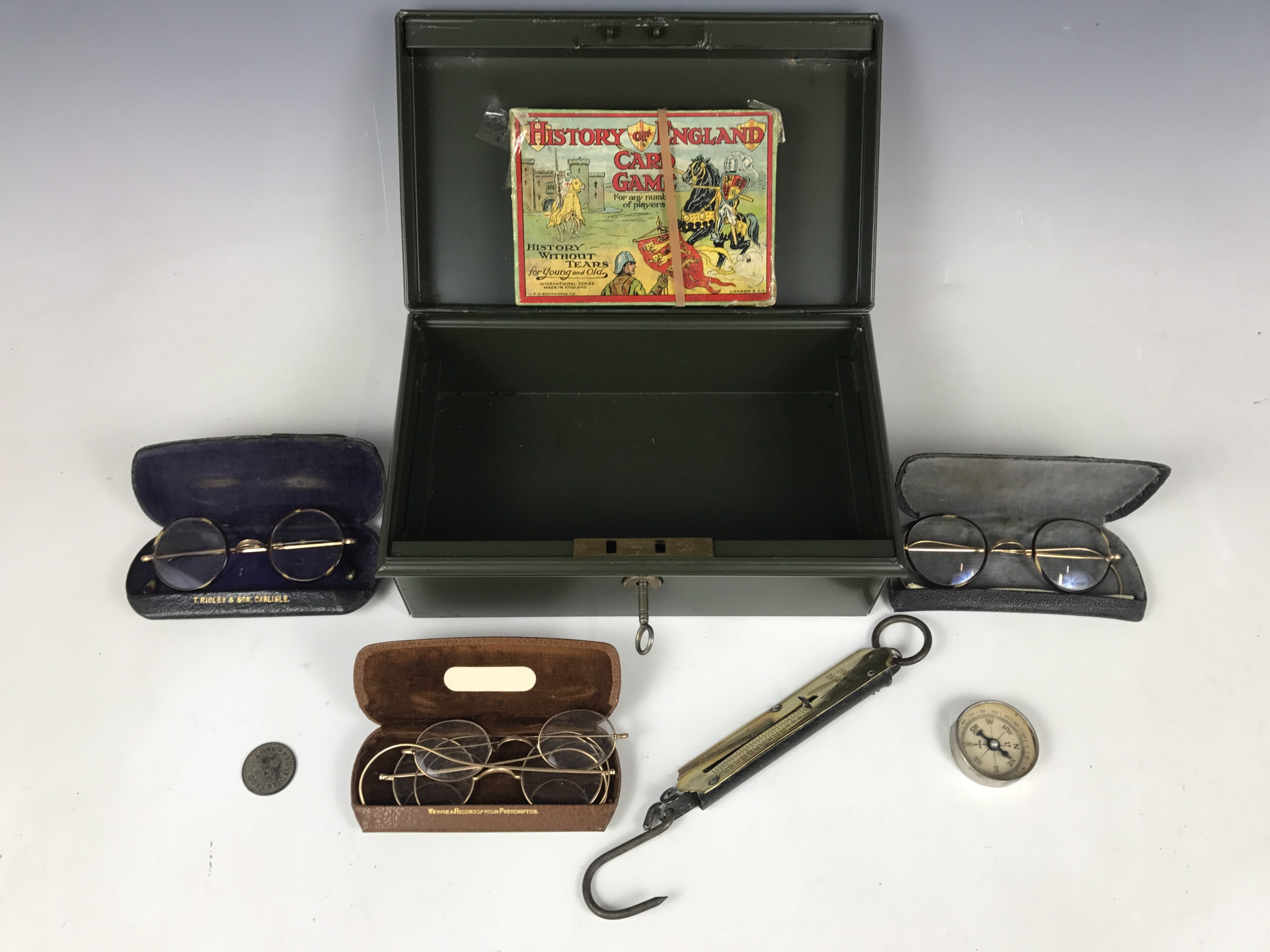 A metal cash box together with pince-nez, spectacles, a pocket balance and a vintage game