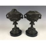 A pair of Victorian spelter covered urns, having polished black slate bases, 21 cm