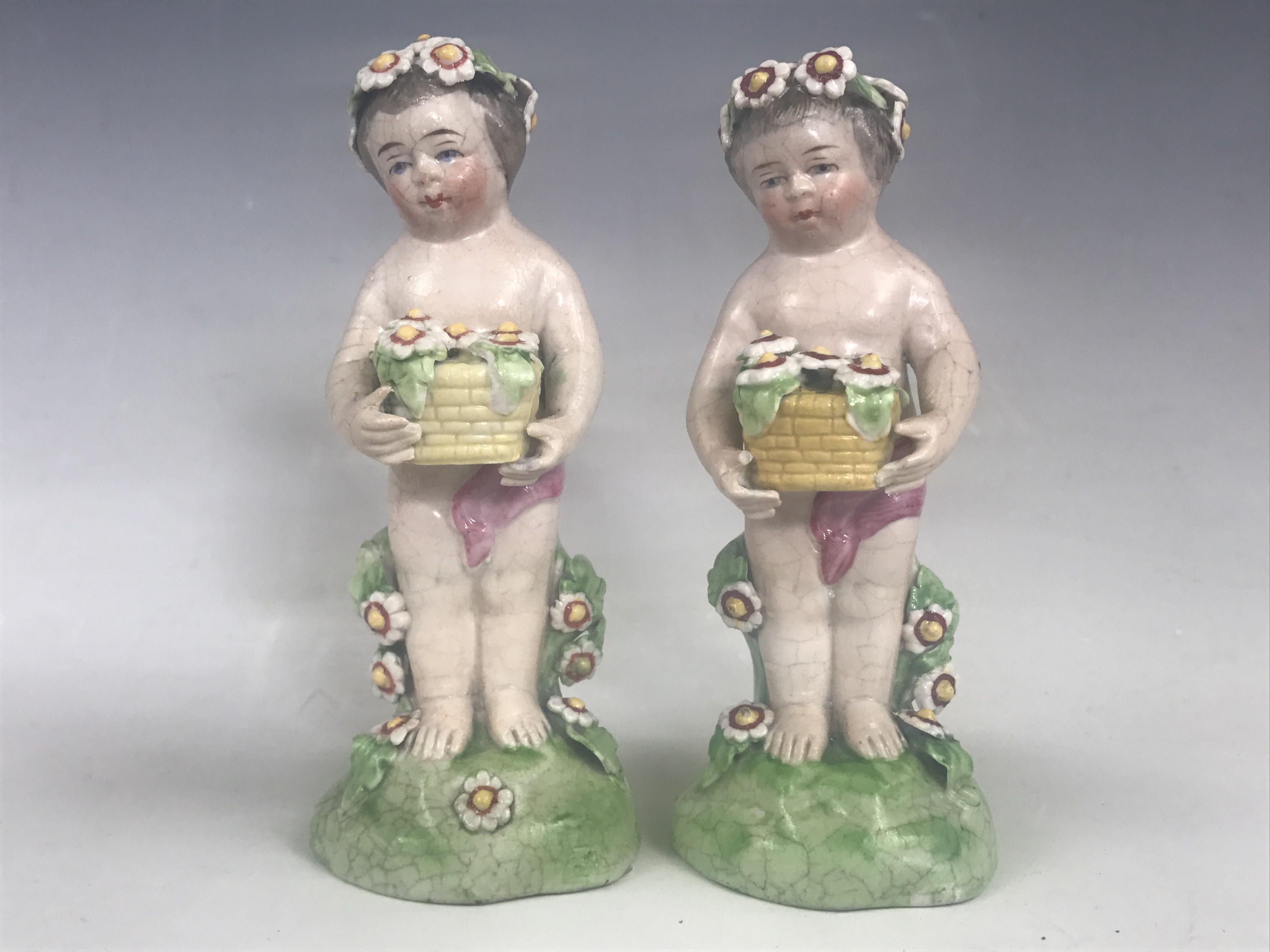 A pair of 19th Century porcelain figurines of putti, each holding aloft a basket of blooms, blue - Image 2 of 3