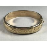 A 9ct gold hinged bangle, the face having foliate engraved decoration, 15.8g
