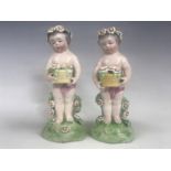 A pair of 19th Century porcelain figurines of putti, each holding aloft a basket of blooms, blue