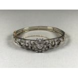 An Edwardian openwork diamond bangle, comprising two blade bars supporting a curvilinear floral