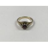 A 9ct gold, garnet and diamond dress ring, having central round-cut garnet flanked by a pair of