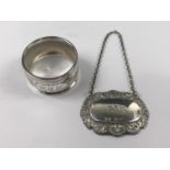 A silver napkin ring together with a silver bottle ticket for 'Gin'