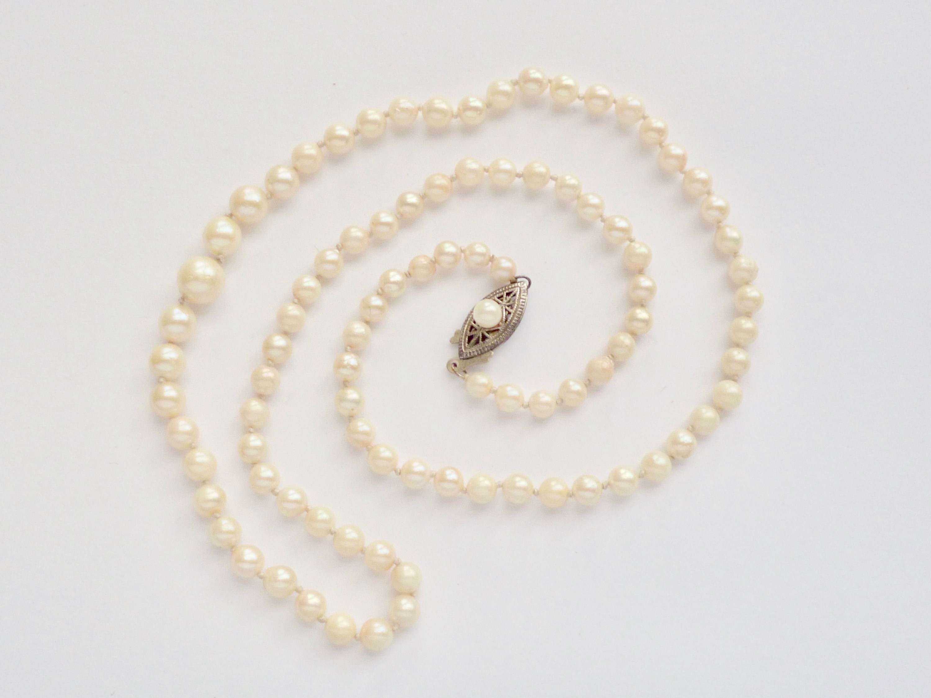 A vintage single-strand necklace of graded pearls, having a white-metal lenticular box-clasp stamped