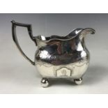 A George III Irish silver cream jug, having an undulating feather-pattern rim, square-shouldered