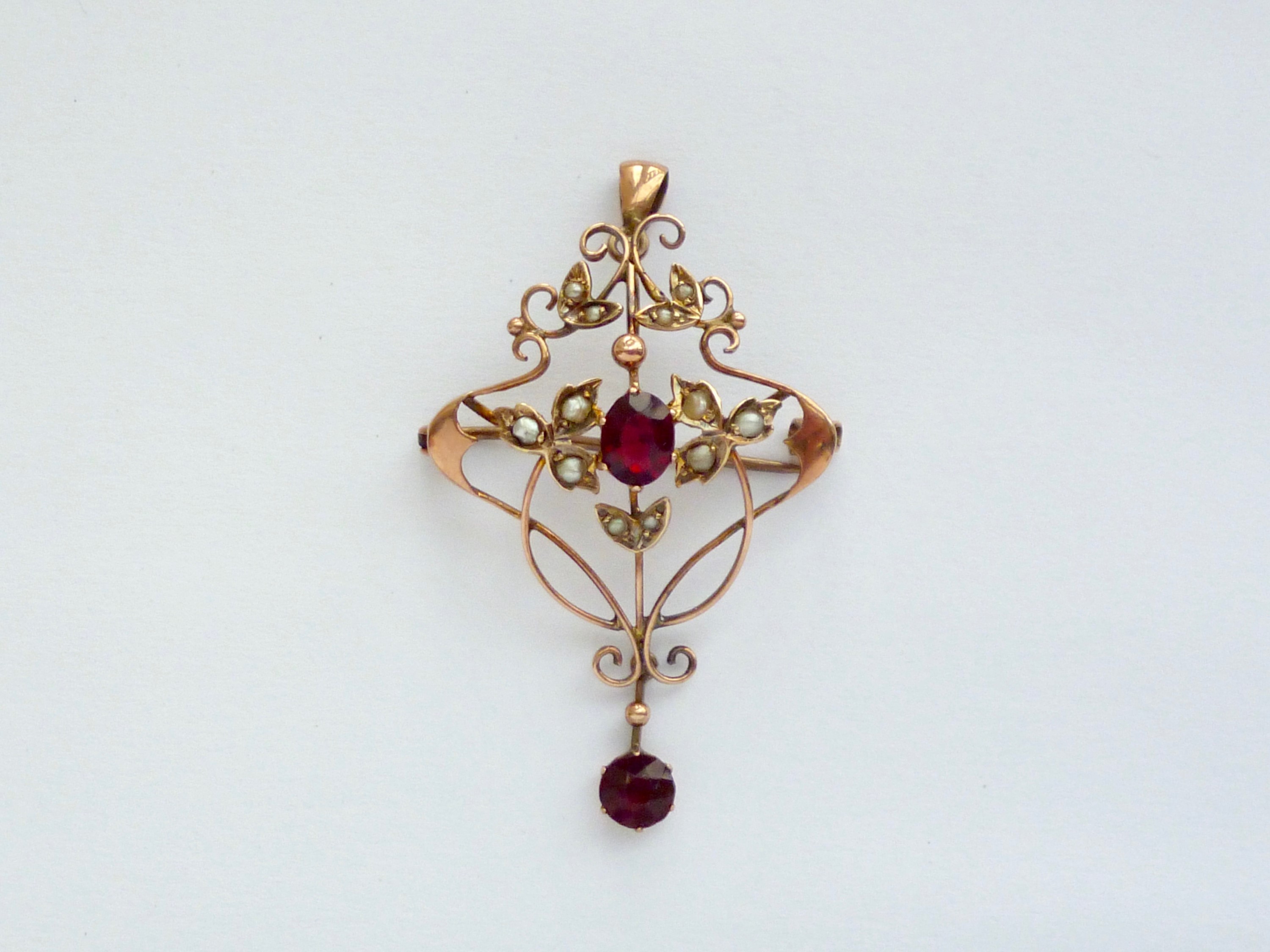 A Belle Epoque yellow-metal, garnet and seed pearl openwork pendant brooch, in a whiplash