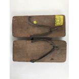 A pair of wooden sandals bearing label with inscription "The type of sandal used in Jap POW camps,