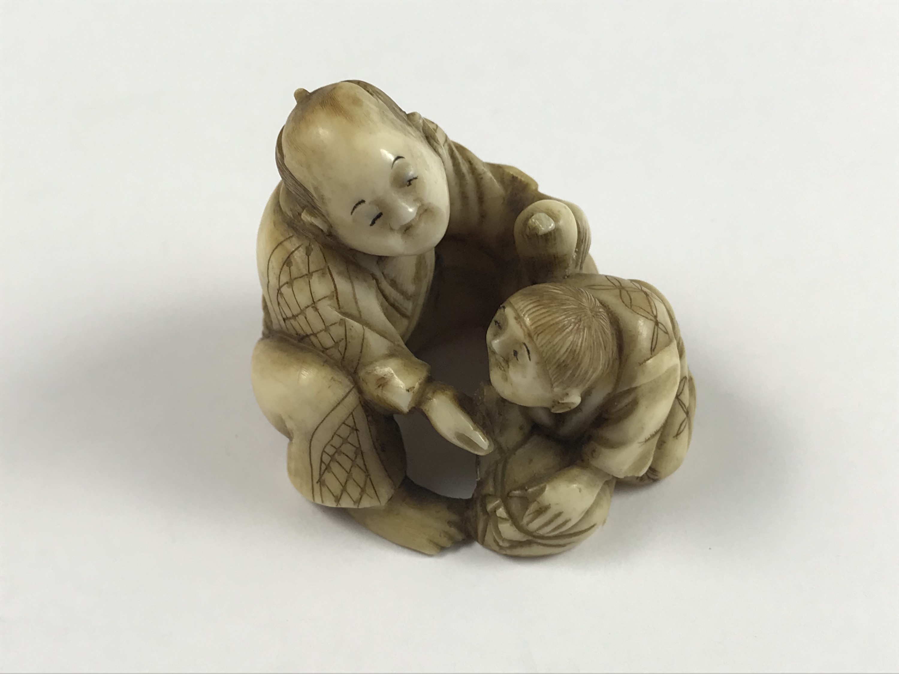 A Meiji Japanese carved ivory netsuke modelled as a crouching man giving assistance to a weary