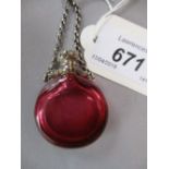 Cranberry glass circular flask shaped perfume bottle with ornate white metal lid and attached chain,