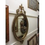 Reproduction oval gilt framed wall mirror with urn and swag surmounts