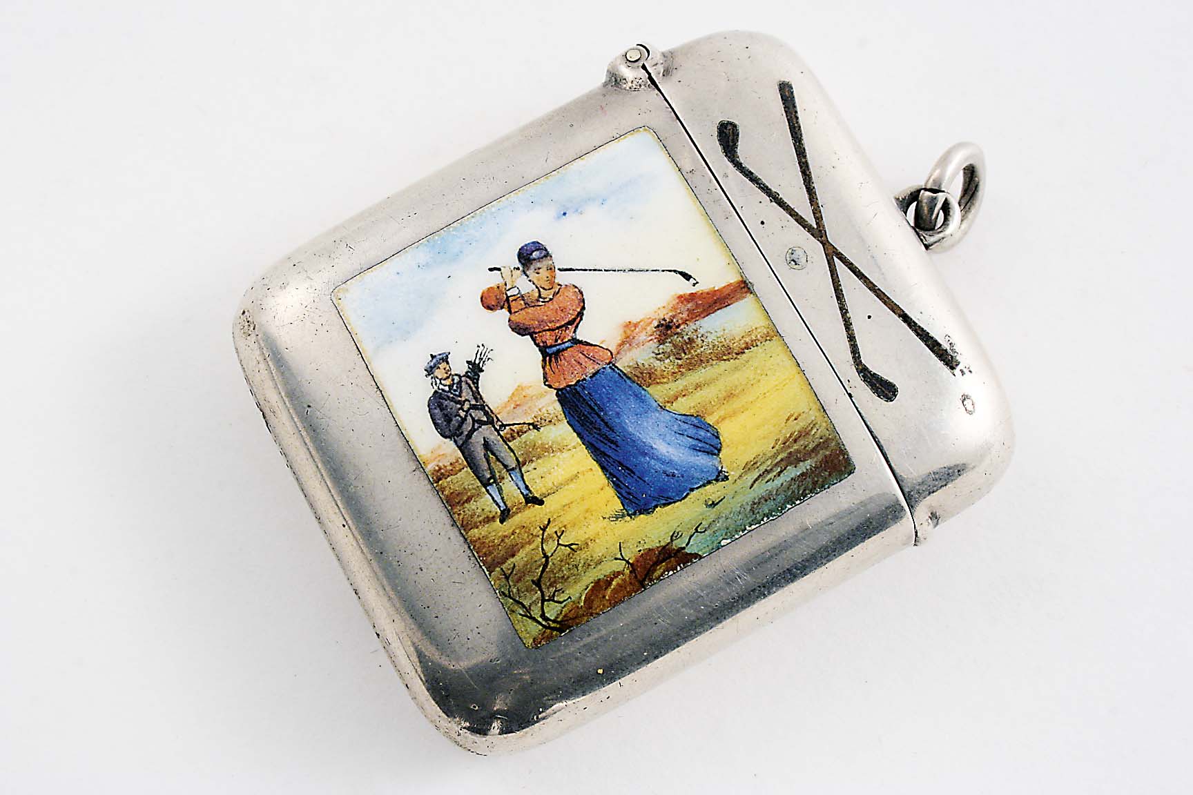 A LATE VICTORIAN SILVER VESTA CASE enamelled on the front with a lady golfer, her caddy and