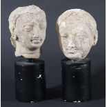 TWO CARVED SCHIST HEADS, South East Asian, on black cylindrical bases, height 19cm and 18cm (2)