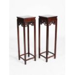 A pair of Chinese tall dark wood jardiniere stands, the square panelled tops above pierced and