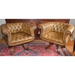A pair of button down leather upholstered revolving tub chairs, with brass studded detail, raised on