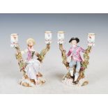 A pair of Meissen porcelain two light candelabra, modelled with male figure wearing puce coloured