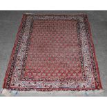 An Eastern madder ground rug, 20th century, the rectangular field decorated with rows of hooked