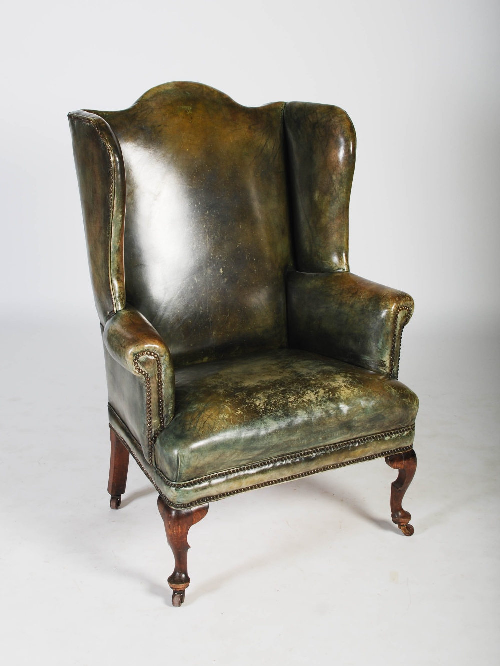 A 19th century oak and green leather upholstered wing armchair, with brass studded detail, raised on