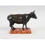 An early 20th century bronze figure of a cow, modelled standing on a mottled red rectangular