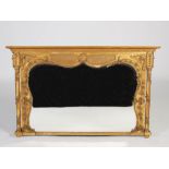 A 19th century gilt wood Rococo style overmantel mirror, the shaped bevelled mirror plate within a