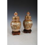 A pair of Japanese Satsuma pottery jars and cover, Meiji Period, decorated with panels of figures on