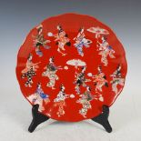 A Japanese porcelain red ground charger, late 19th/early 20th century, decorated with procession
