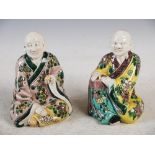 Two Chinese porcelain figures of monks, one sitting with crossed legs holding a fruit in his left