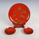 A Japanese red ground lacquer footed dish on dark wood stand and two smaller matching dishes,