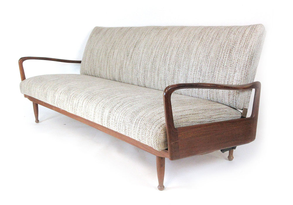 A 1970's teak framed daybed with cream speckled upholstery, the arms of organic form,