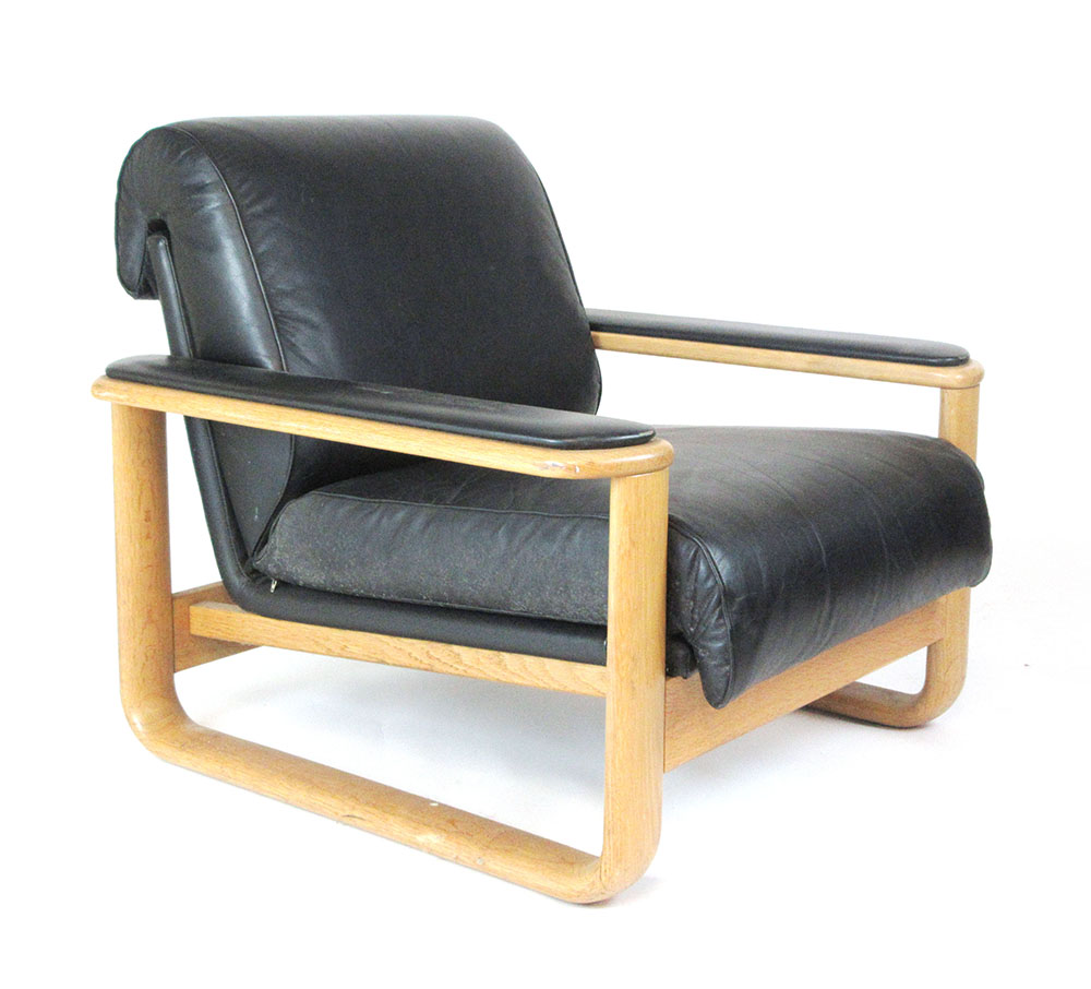 A 1970's oak framed low lounge armchair with black leather armpads and upholstery on a sleigh-type