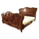 A late 19th/early 20th century French walnut double bed with asymmetric scroll carving to the foot