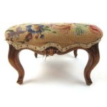 A Victorian walnut footstool upholstered in a needlework fabric over the carved rails with shell