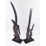 CHIWARA, a companion pair, carved wood with metal embellishments, 66cm H and 77cm H.