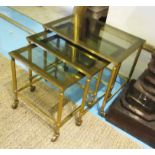 NEST OF TABLES, a set of three graduated gilt metal framed, each with a glass top on wheels,
