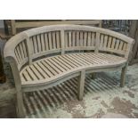 'BANANA' GARDEN BENCH, weathered teak of slatted construction, of curved form and rounded back,