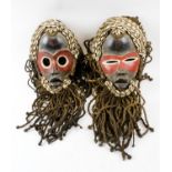 TWO DAN FACE MASKS, both carved and painted wood with cowrie shell ornamentation and sisal fringes,
