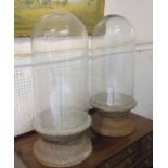 GLASS DOMES, a pair, each on a raised metal socle base, 75cm H.