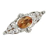 A topaz and diamond set broochmillegrain set with an oval cut orange topaz, in an open scrolling