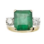 An emerald and diamond set ringclaw set with a square trap cut emerald, flanked to either side by