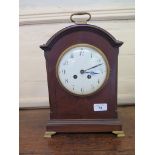 An Edwardian mahogany mantel clock, with brass handle over an arched case and enamel dial on brass