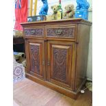 A late Victorian ornately carved walnut side cabinet, with two frieze drawers over a pair of