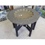 An Eastern brass dished table, on a carved wood folding base, 77cm diameter