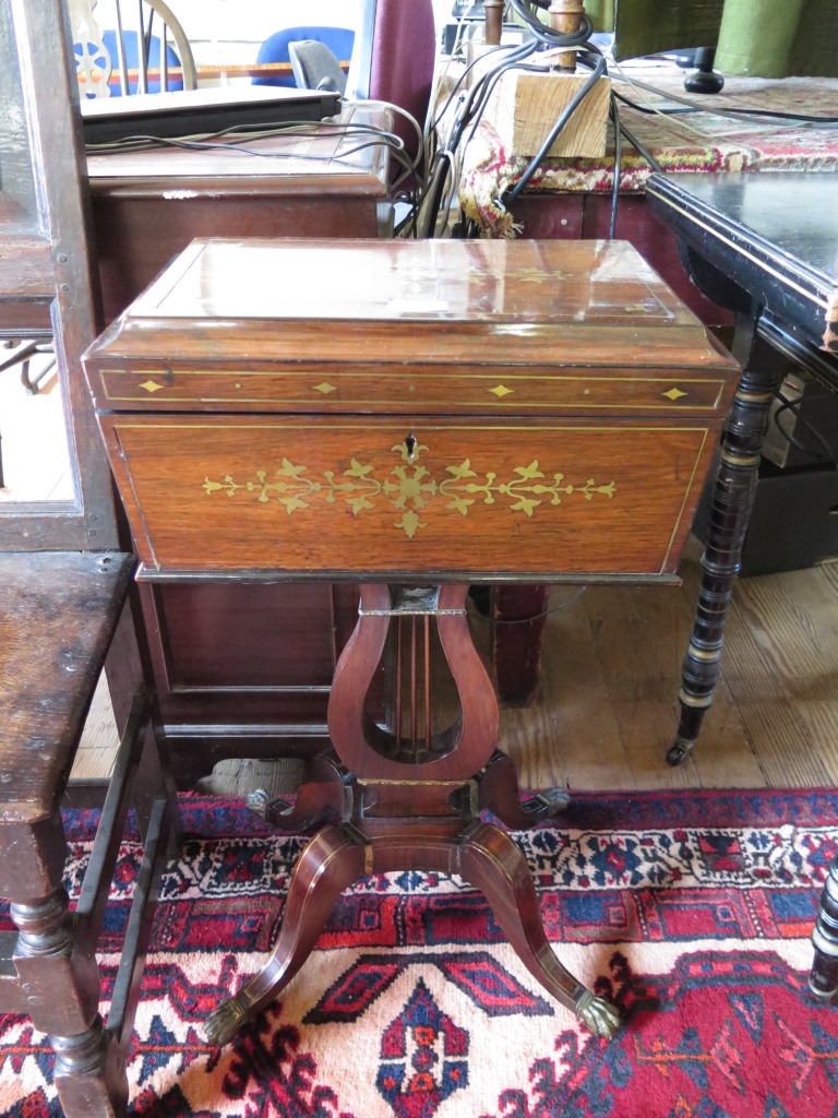 A Regency rosewood and brass inlaid teapoy, with ring handles, the hinged lid enclosing four caddies