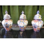 A set of three Japanese Imari vases and covers, with domed lids and octagonal bodies depicting bowls