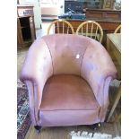A pink upholstered tub armchair, with turned feet and castors