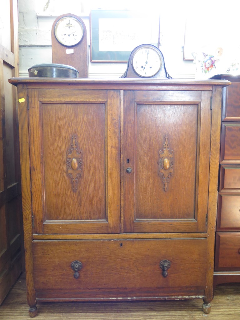 A 1930s oak cabinet, the twin panelled and cabochon applied doors over a long drawer on turned feet,