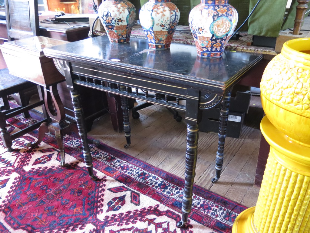 A Victorian ebonised foldover card table in the Aesthetic style with gilt highlights, the spindle