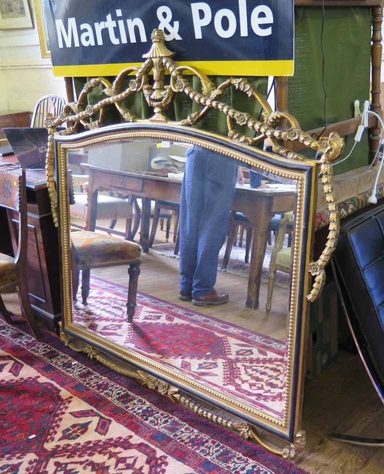 An ebonised and giltwood over mantel mirror, the arched bevelled plate with a beaded frame