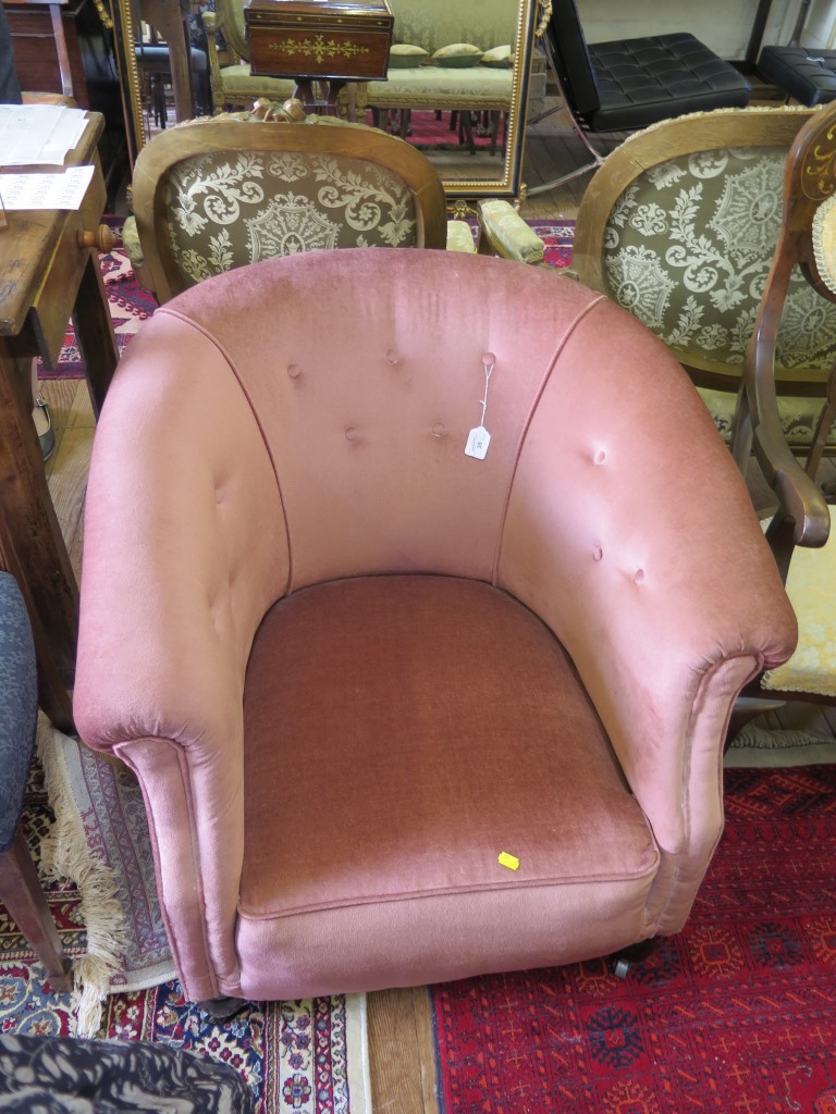 A pink upholstered tub armchair, with turned feet and castors