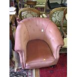 A pink upholstered tub armchair, with turned feet and castors